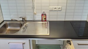 Una cocina con un lavamanos de acero inoxidable, una encimera negra, un horno integrado y un escurreplatos.