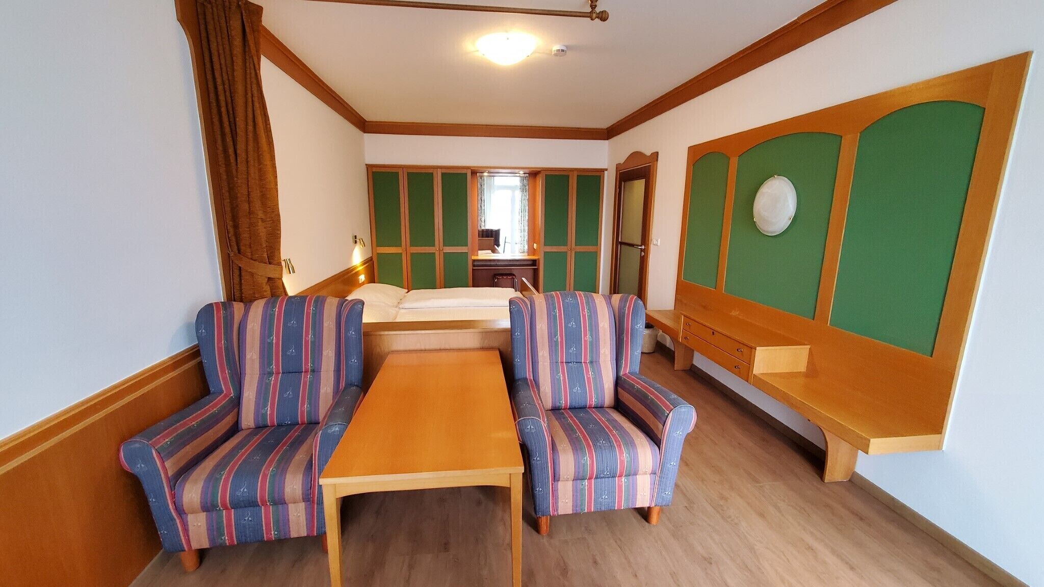 A room with a wooden table, striped armchairs, a bench, and a green panel wall.