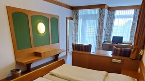 A hotel room with a double bed, a desk with a chair, a television, and a window with curtains. - Apartment 304, apartment, 38 sqm, 1-2 persons, balcony (Bad Reichenhall)
