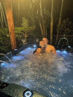 Un jacuzzi con dos personas, rodeado de bambú y otras plantas tropicales.