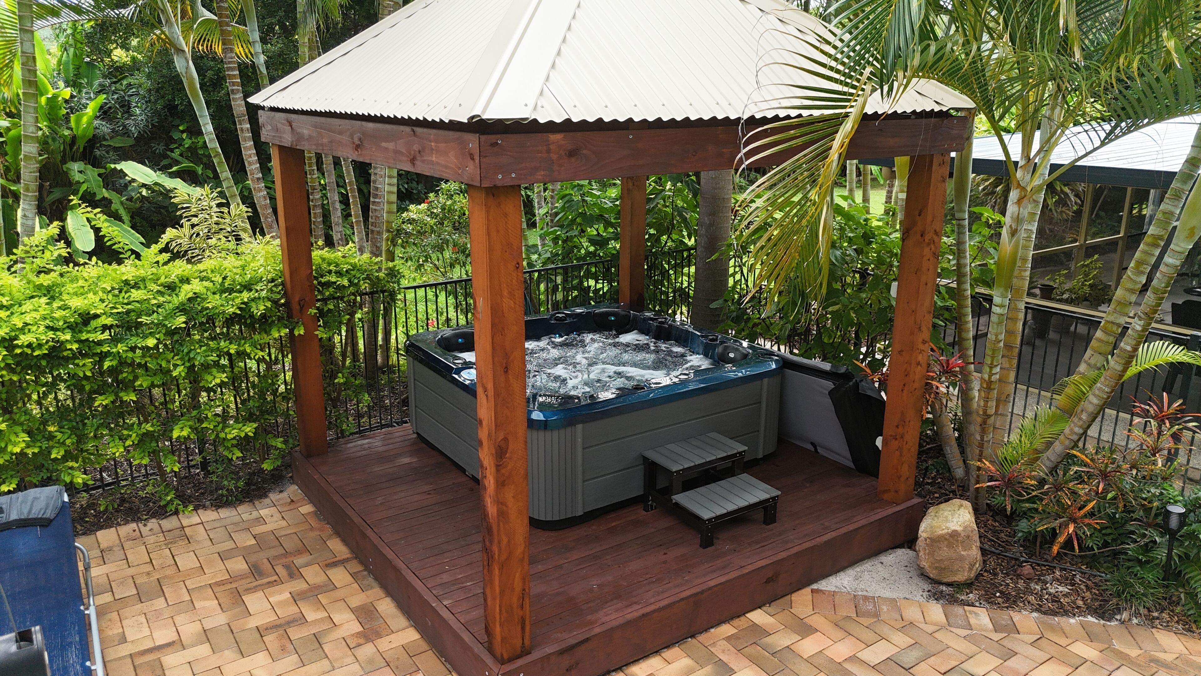 A hot tub in a gazebo surrounded by lush greenery.