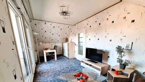 Ein Wohnzimmer mit Fernseher, Glastisch, Sofa, Esstisch und Schrank.