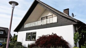 Ein modernes, zweistöckiges Haus mit geneigtem Dach, einem Balkon und einer Satellitenschüssel.