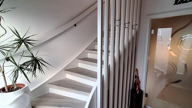 Eine Wendeltreppe mit weißen Stufen und einer Zimmerpflanze auf der linken Seite.