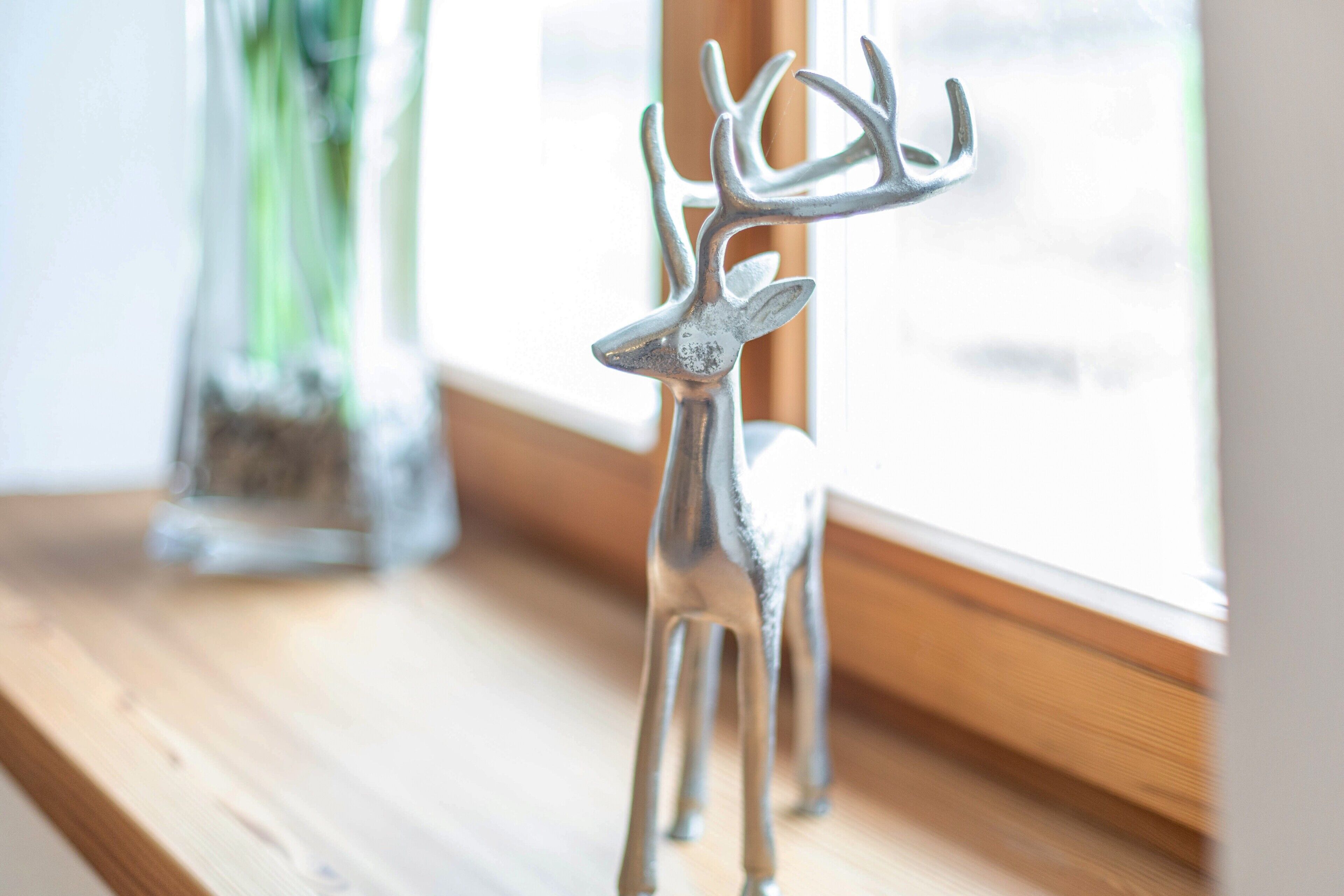 Eine Metall-Hirschfigur auf einer Holzoberfläche in der Nähe eines Fensters.