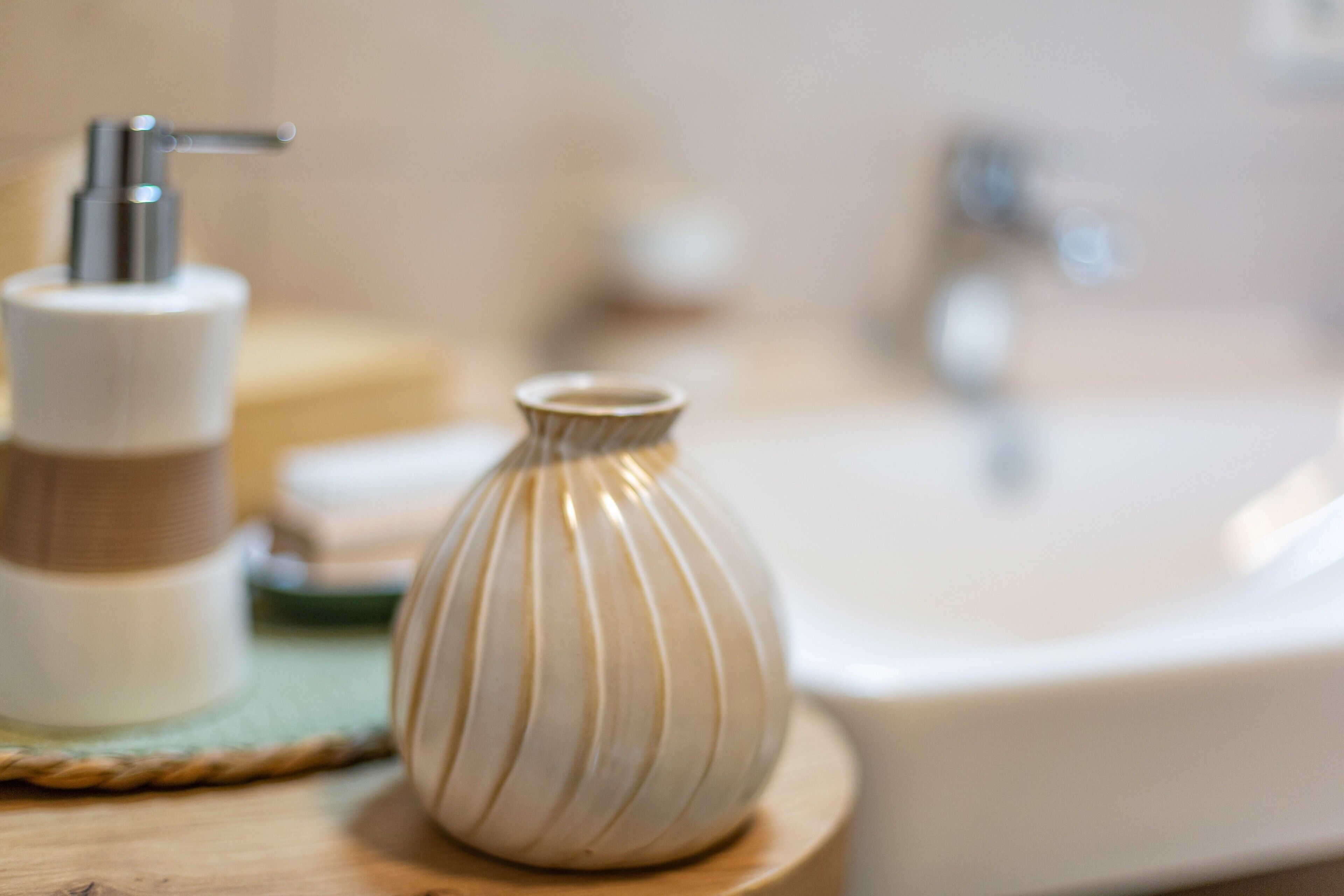Un baño con lavabo, dispensador de jabón y un florero sobre una superficie de madera.