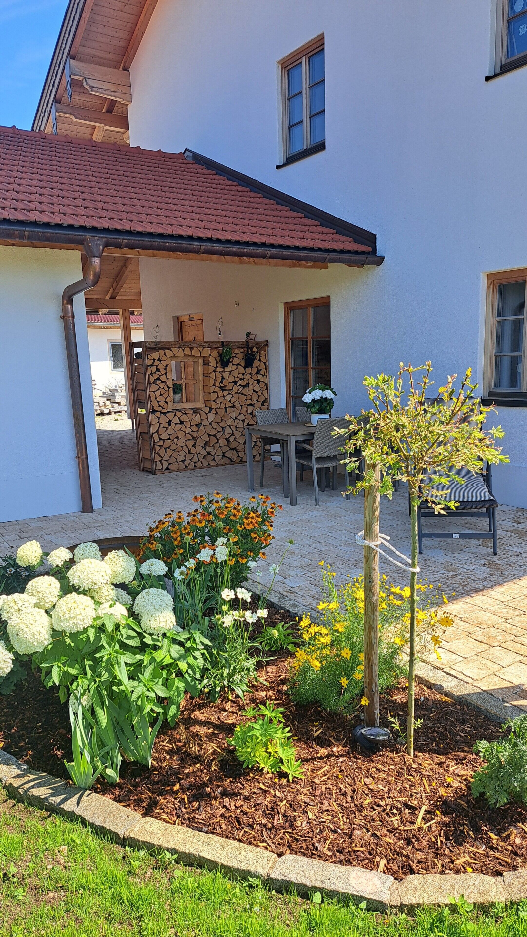 Una casa con porche cubierto, mobiliario exterior y un jardín con flores y plantas.