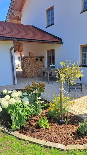 Une maison dotée d’un patio couvert, d’un espace salon extérieur et d’un jardin agrémenté de fleurs et de plantes.