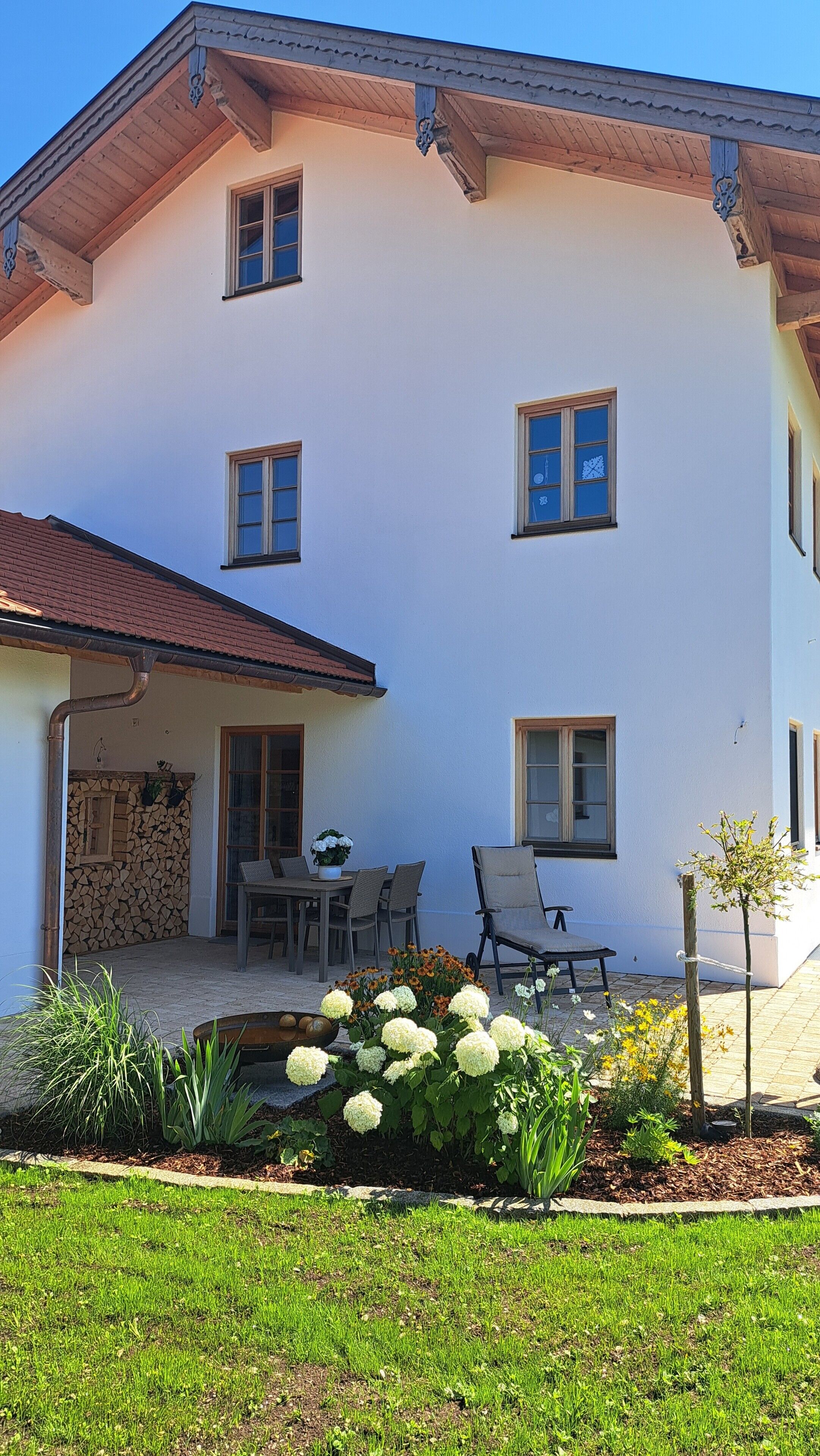 A two-story building with a balcony, a stone wall, and a garden with flowers and plants.