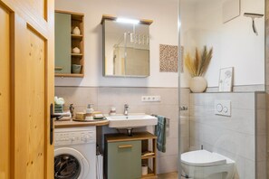 Een praktische badkamer met een wasmachine, wastafel, toilet en spiegel.