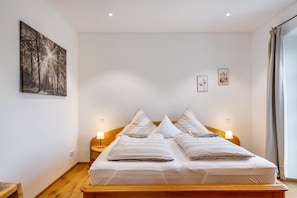 Un lit double avec deux oreillers, une table de chevet avec une lampe, une tête de lit en bois, un tableau accroché au mur et une fenêtre avec des rideaux.