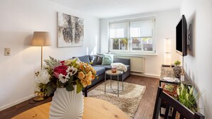 A living room with a sofa, a small round table, a vase with flowers, a lamp, and a television mounted on the wall. - Holiday Apartment 'Terrassenwohnung' with Private Terrace and Wi-Fi (Rötha)