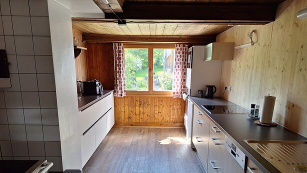 A kitchen with wooden cabinets, a countertop, and a window with curtains. - Apartment 'Ferienwohnung in Altem Bauernhaus' with Mountain View, Private Garden and Wi-Fi (Schwarzenberg)