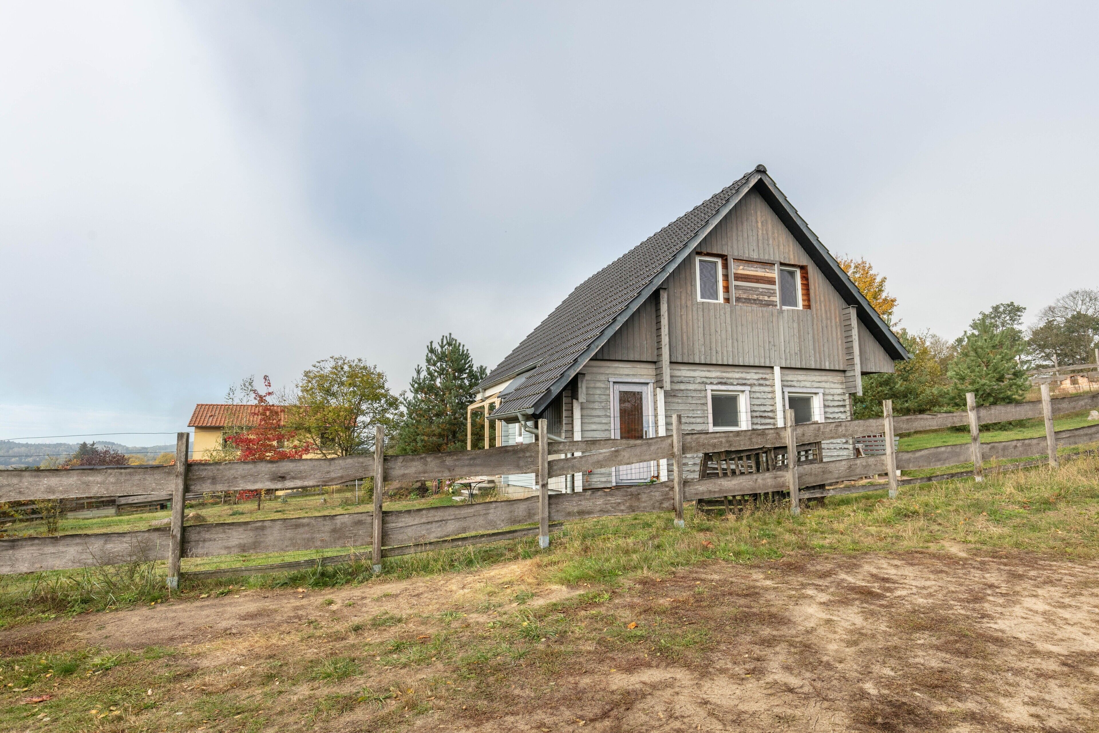 Une maison rustique en bois, avec un toit en pente, une clôture en bois et un chemin de terre qui y mène.