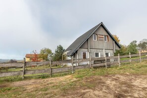 Une maison rustique en bois, avec un toit en pente, une clôture en bois et un chemin de terre qui y mène.
