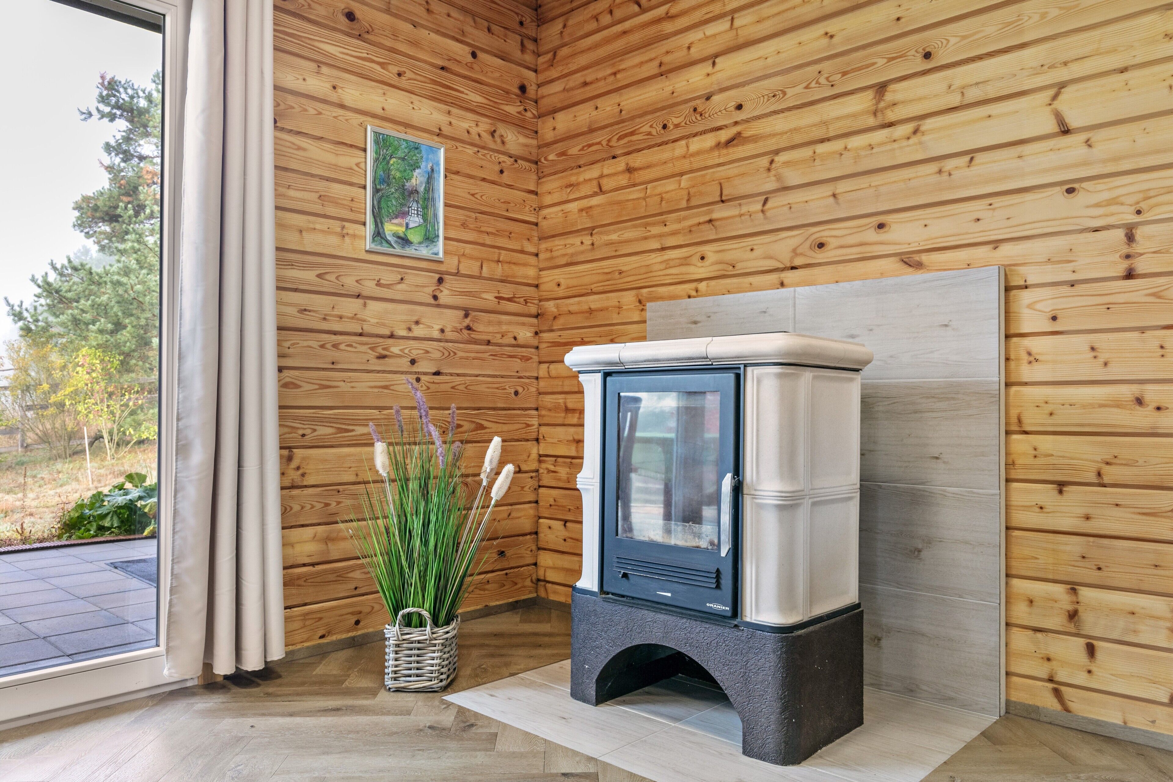 L’intérieur d’un chalet en bois, avec un poêle à bois, une fenêtre avec des rideaux et un tableau accroché au mur.