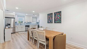 Een moderne keuken met witte kastjes, een roestvrijstalen koelkast, en een eetgedeelte met een houten tafel en stoelen.