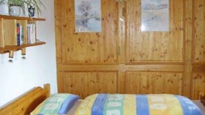 Ein Zimmer mit Holzwänden, einem Bett, einem Bücherregal und zwei gerahmten Bildern an der Wand.