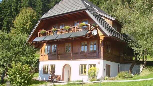 Eine Holzchalet mit Balkon, Eingangstür und kleiner Veranda.