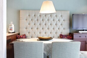 A room with a tufted headboard, a television, a table with a bowl, patterned chairs, and a lamp.