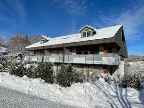 A modern two-story building with a sloped roof, large windows, and a balcony.