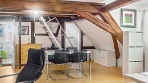 A room with a wooden ceiling, a table with chairs, a ladder, a radiator, and a framed picture on the wall. - Apartment 'Alte Schmiede Ellrichshausen' with Wi-Fi (Satteldorf)