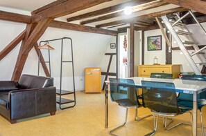 Ein Zimmer mit einem Schlafplatz auf Erker, einem Schreibtisch mit Stühlen, einem kleinen Kühlschrank und einer Leiter.
