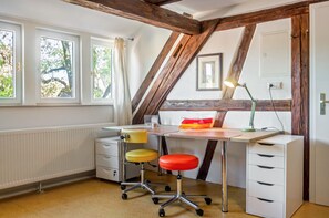 Ein Zimmer mit Schreibtisch, zwei Stühlen, einer Heizung und einem fenster mit Vorhängen.