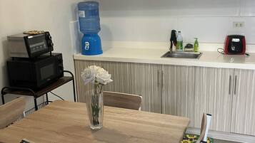 A compact kitchen with white cabinets, a microwave, a water dispenser, and a sink.