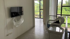 A room with a TV mounted on the wall, a wicker chair, and a view of greenery through large windows. - Peaceful Valencia Dream Home (Valencia)