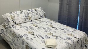 A bedroom with a bed, a wall-mounted fan, a green shelf, and a window with a curtain. - Peaceful Valencia Dream Home (Valencia)