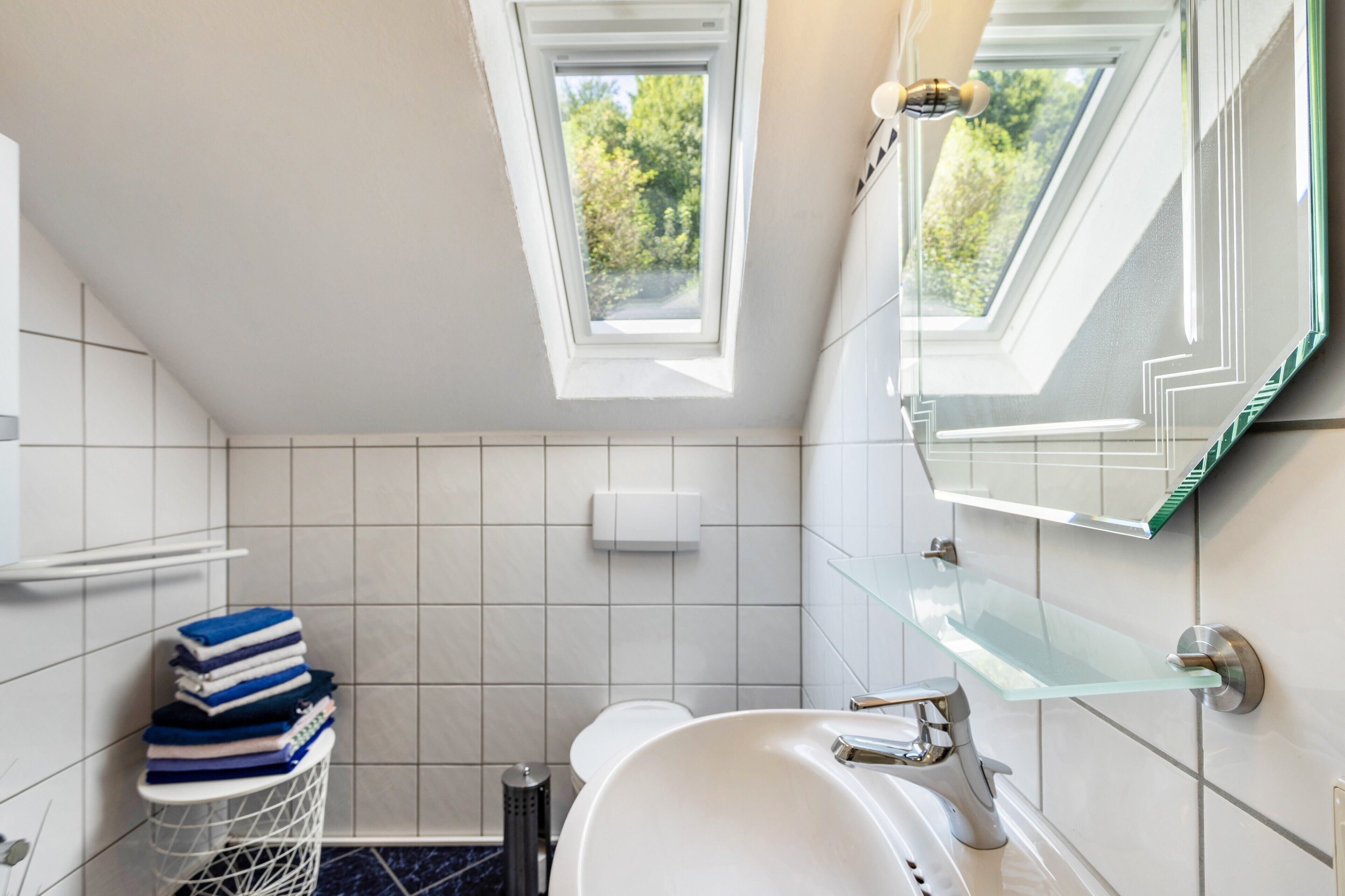 Et badeværelse med ovenlys, håndvask, toilet og en glashylde.
