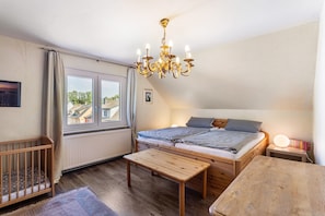Une chambre avec un lit en bois, une petite table de chevet, une commode, une fenêtre avec des rideaux, un lustre et une vue sur les bâtiments environnants.