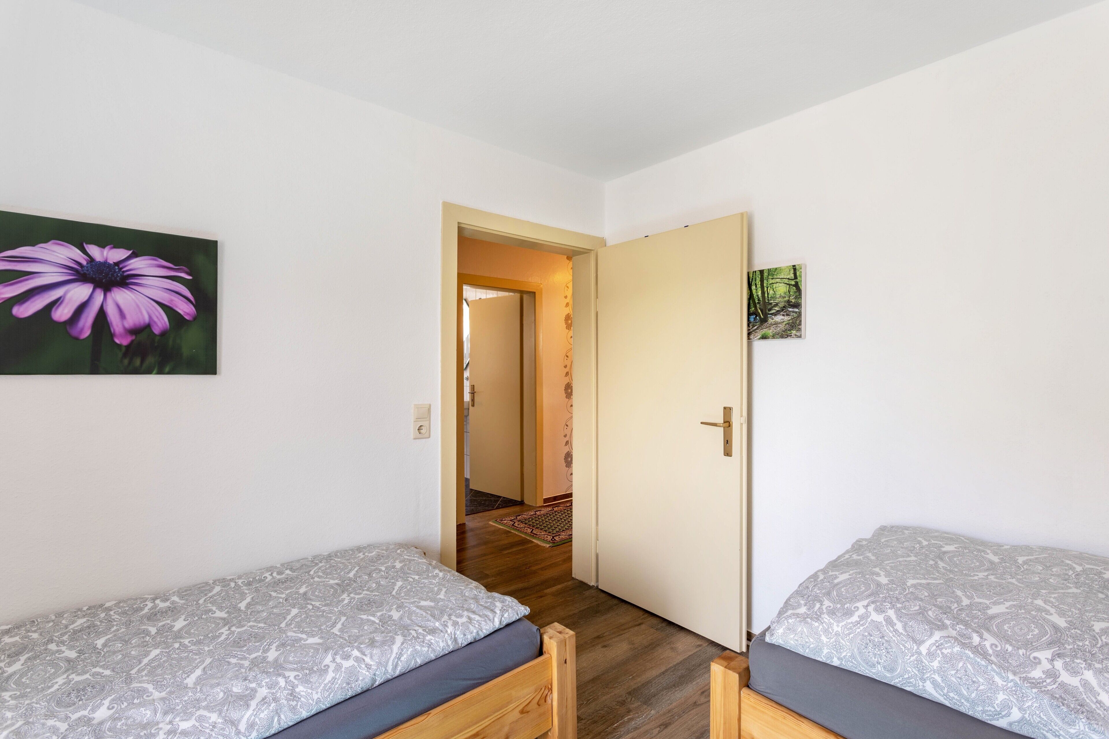 A room with two single beds, a door leading to another room, and a wall-mounted picture of a flower.