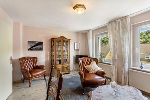 Une pièce comprenant deux fauteuils en cuir, un meuble en bois, un téléviseur et une fenêtre avec des rideaux.