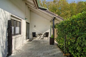 A covered patio area with a table and chairs, a potted plant, and a hedge. - Apartment 'Möwe' with Private Terrace, Garden, and Wi-Fi (Hinte)
