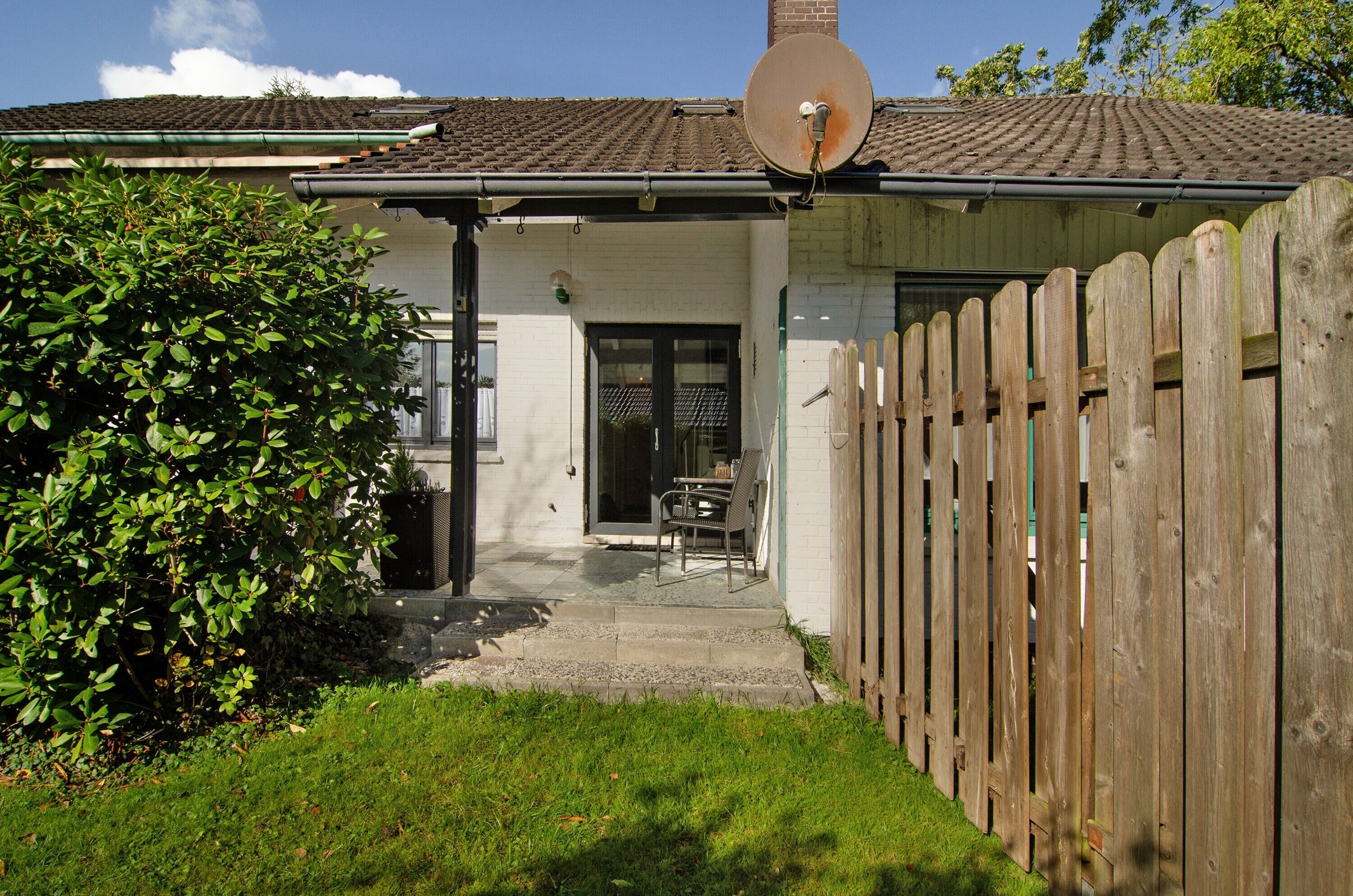 Una casa con un'antenna parabolica, una recinzione in legno e un piccolo patio con tavolo e sedie.