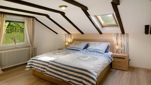 A bedroom with a sloped ceiling, a bed with striped bedding, a nightstand, a bedside lamp, and a window with curtains. - Apartment Möwe with Private Terrace, Fenced Garden & Wi-Fi (Hinte)