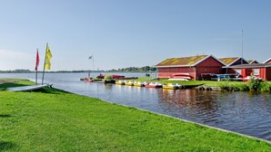 A lakeside view with boats docked, red buildings, and a grassy area. - Apartment Möwe with Private Terrace, Fenced Garden & Wi-Fi (Hinte)