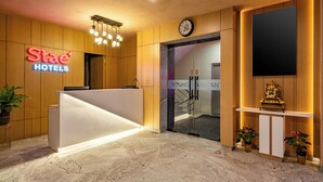 A hotel reception area with a modern design, featuring a reception desk, a clock, and a television screen. - Stae Hotels (Hyderabad)