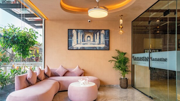 A modern lobby with a pink sofa, a round ottoman, and a large painting of an architectural corridor. - Stae Hotels (Hyderabad)