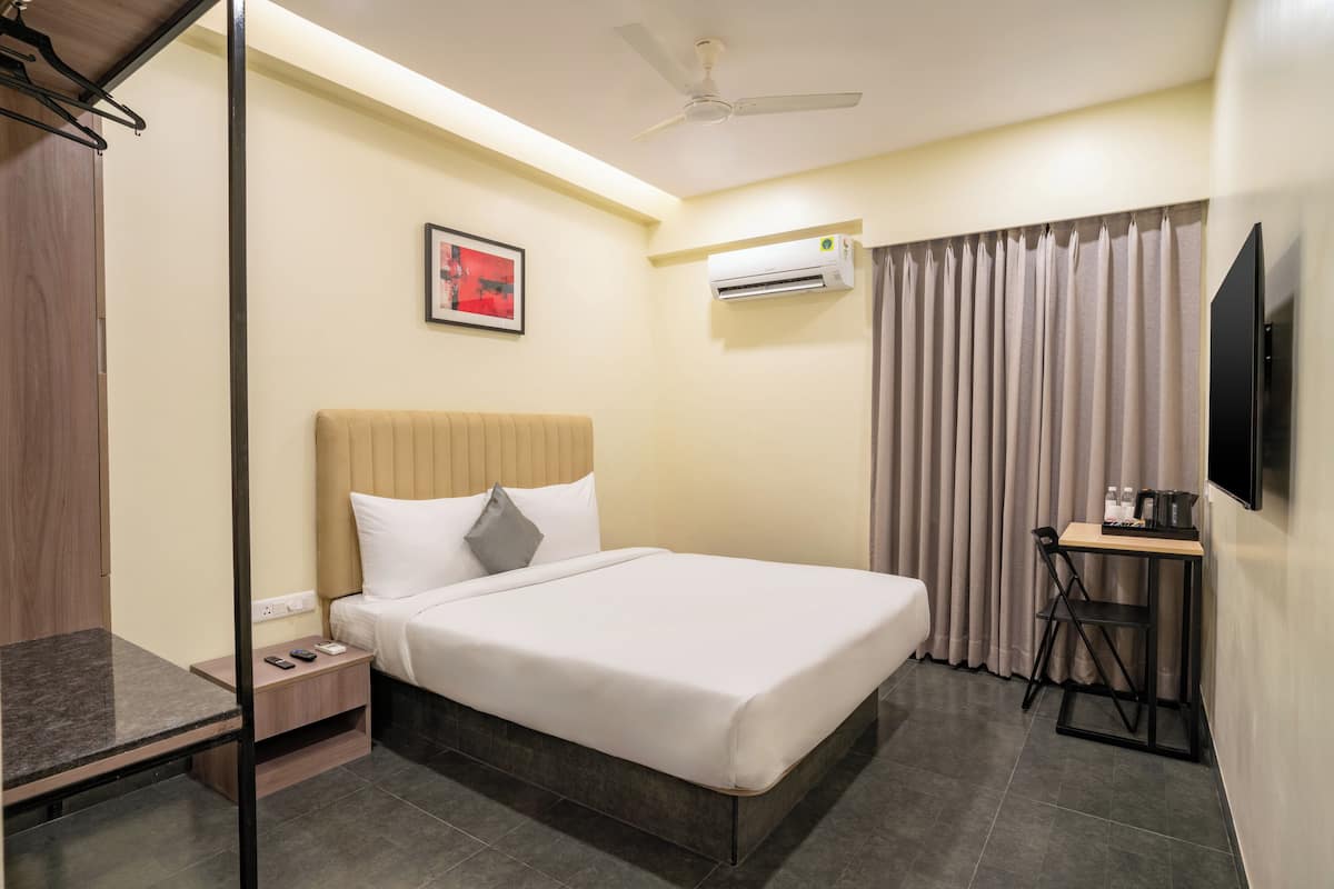 Una habitación de hotel con cama, mesita de noche, silla, televisor, aire acondicionado y cortinas.