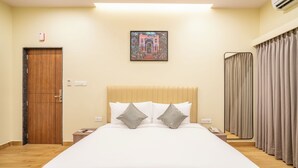 A hotel room with a large bed, a wooden door, a nightstand, a telephone, and a window with curtains. - Stae Hotels (Hyderabad)