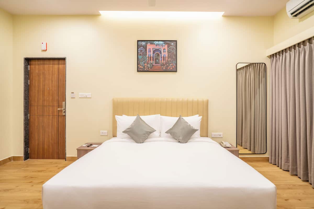 Habitación de hotel con una cama grande, una puerta de madera, una mesita de noche, un teléfono y una ventana con cortinas.