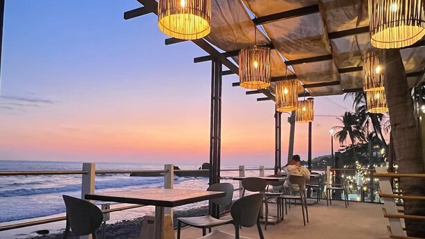 An outdoor seating area with tables and chairs, overlooking the ocean at sunset.