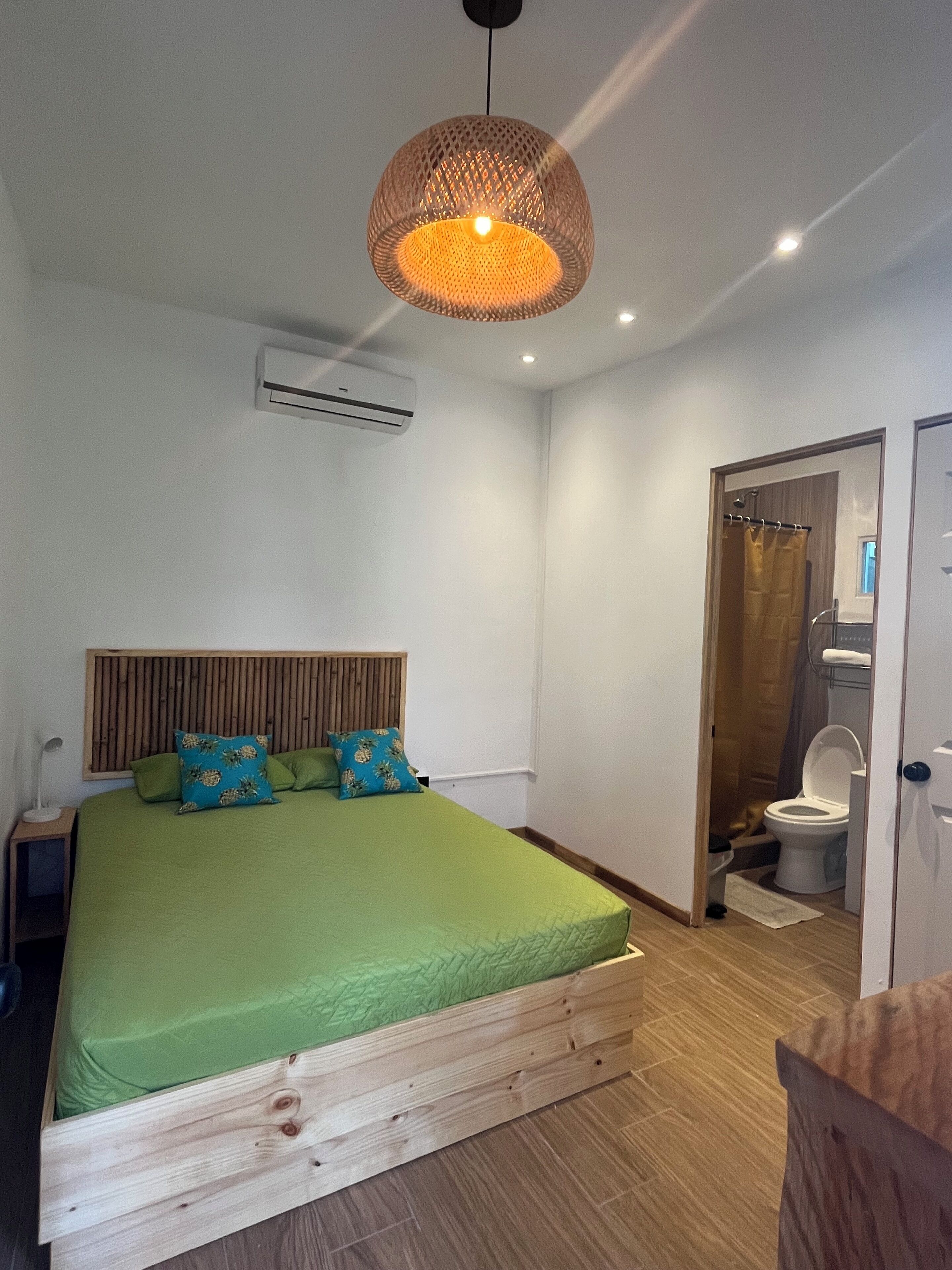 A bedroom with a wooden bed frame, a green bedspread, and a hanging light fixture.