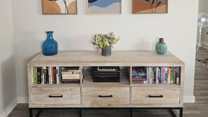 Une console en bois, ornée de livres, d’un vase de fleurs et de trois œuvres d’art encadrées accrochées au mur.
