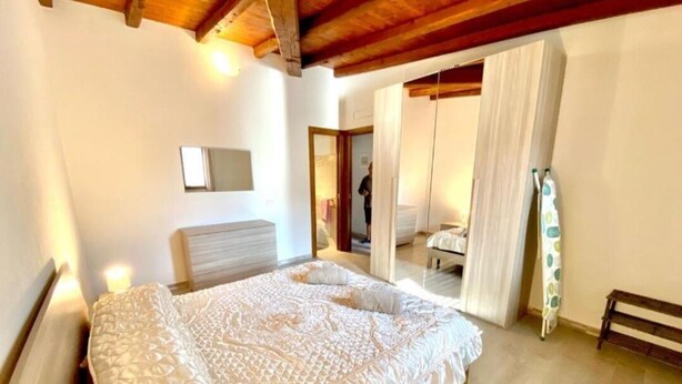 Een slaapkamer met een groot bed, een houten plafond, een nachtkastje en een spiegel aan de muur.