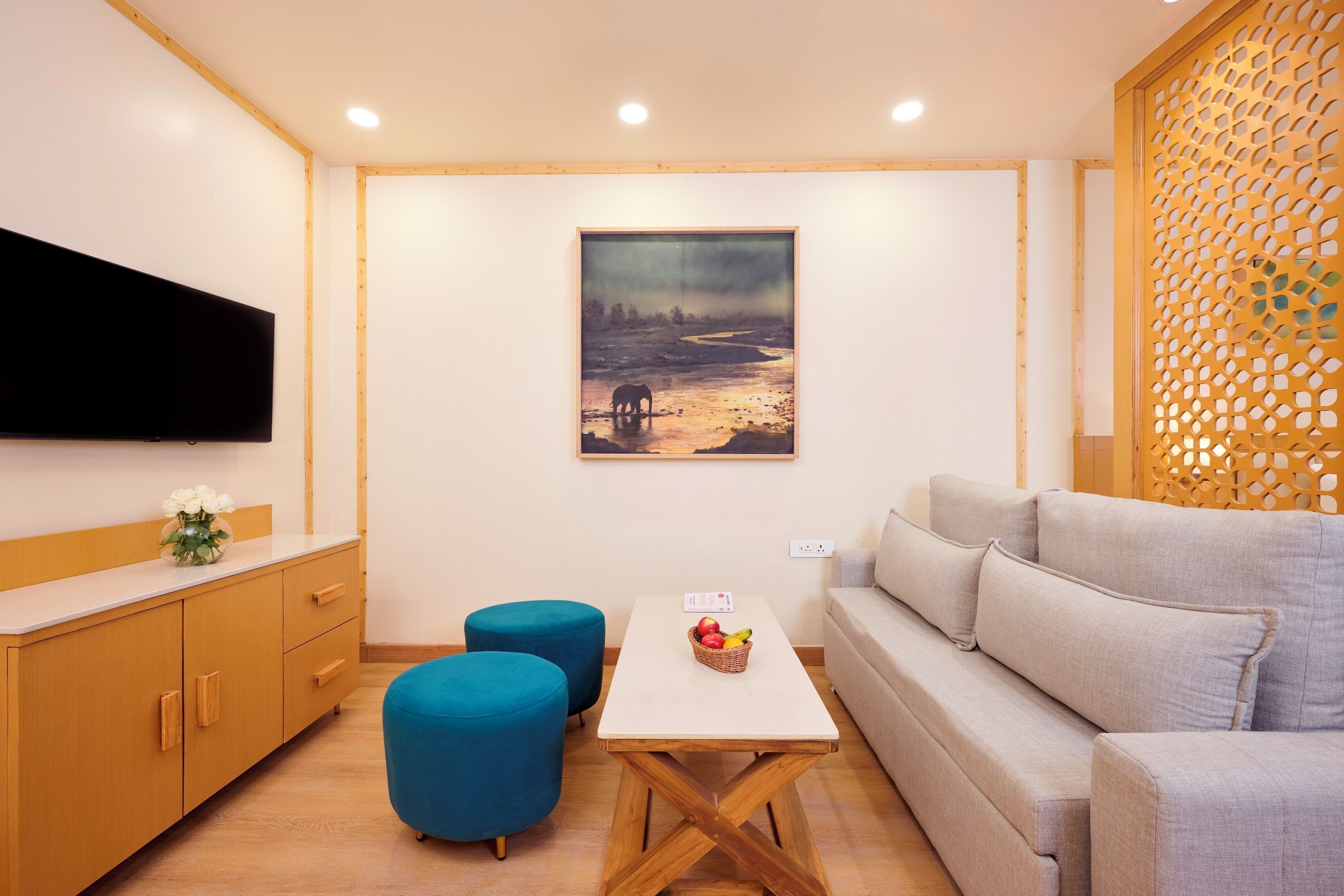 Una sala de estar moderna con una televisión de pantalla plana, un cuadro, un sofá, una mesa con una cesta de fruta y un otoman azul.