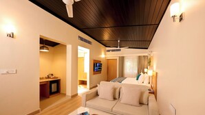 A modern hotel room with a wooden ceiling, a sofa, a coffee table with a basket, and a TV on the wall. - ABN Sarovar Portico Jim Corbett  (Ramnagar)